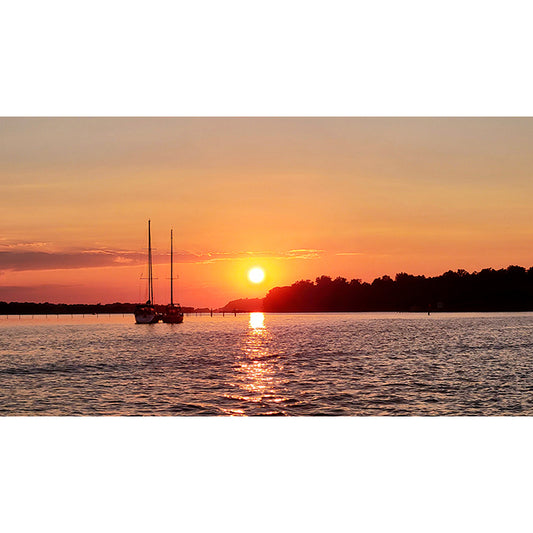 Photographic artwork by Jessica St. Clair depicting two sailboats savoring the soft glow of a setting sun as they settle in for a serene night on the river.