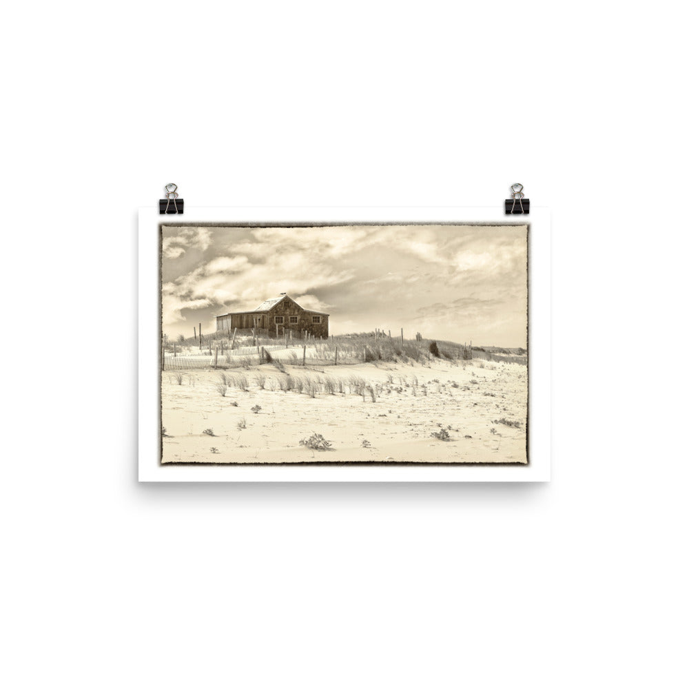 Image of The Retreat mixed media sepia tone artwork on 12 inch by 18 inch premium matte photo paper by Jessica St. Clair depicting a weathered beach cottage in the sand beside the ocean with two seagulls perched atop the roof