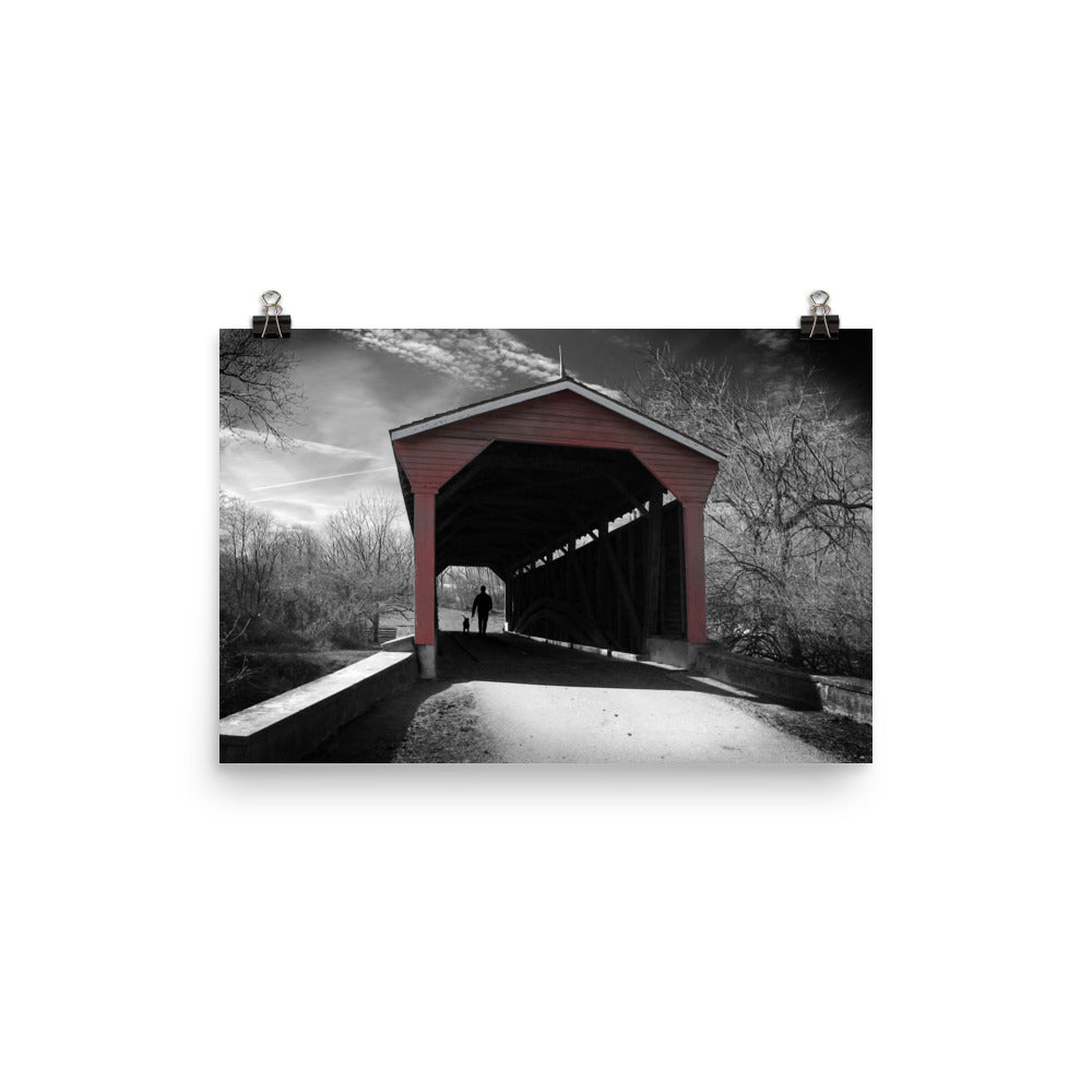 Image of Winter in Fair Hill 12 inch by 18 inch art print depicting a black and white winter scene with a man and dog in silhouette walking through a red covered bridge.
