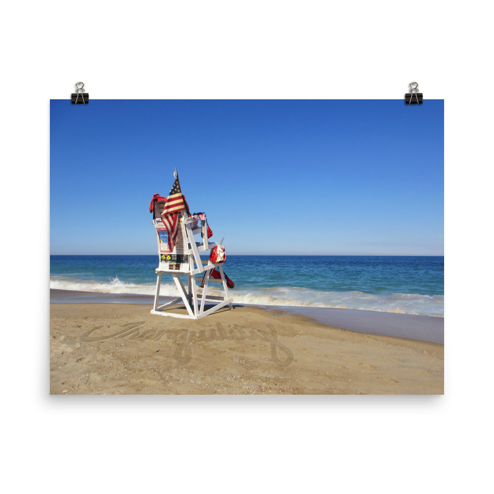 Image of Tranquility photographic art print on 18 inch by 24 inch premium luster photo paper by Jessica St. Clair depicting a lifeguard stand with an American flag overlooking calm ocean water with the word tranquility written in the sand